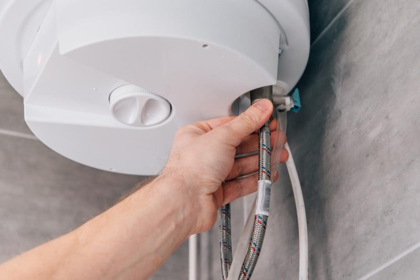 Tecnico che controlla i tubi flessibili sotto uno scaldabagno elettrico